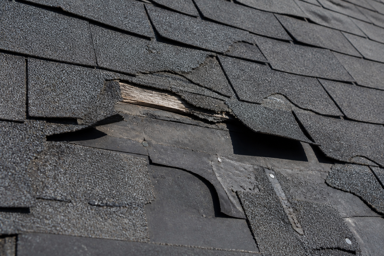 close-up of real roof damage signs — worn, cracked shingles on a residential roof